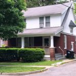 Exterior of two story house with large covered front porch, red brick, and white cedar shake shingles