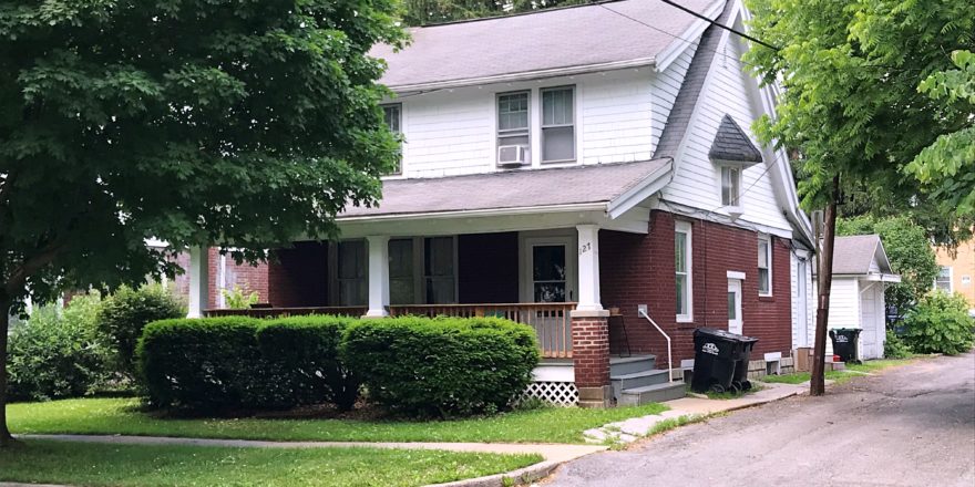 Exterior of two story house with large covered front porch, red brick, and white cedar shake shingles