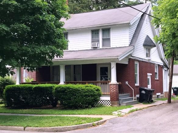 Exterior of two story house with large covered front porch, red brick, and white cedar shake shingles