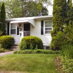 Exterior of a home with white siding, black shutters, and covered front entry.