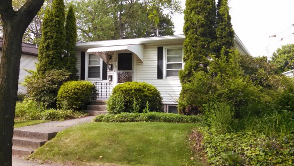 Exterior of a home with white siding, black shutters, and covered front entry.