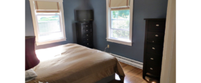 Bedroom with queen bed and two black dressers with 5 drawers. A TV is on top of one of the dressers.