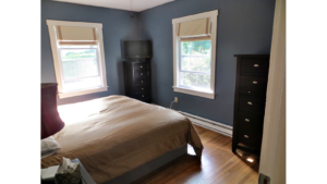 Bedroom with queen bed and two black dressers with 5 drawers. A TV is on top of one of the dressers.