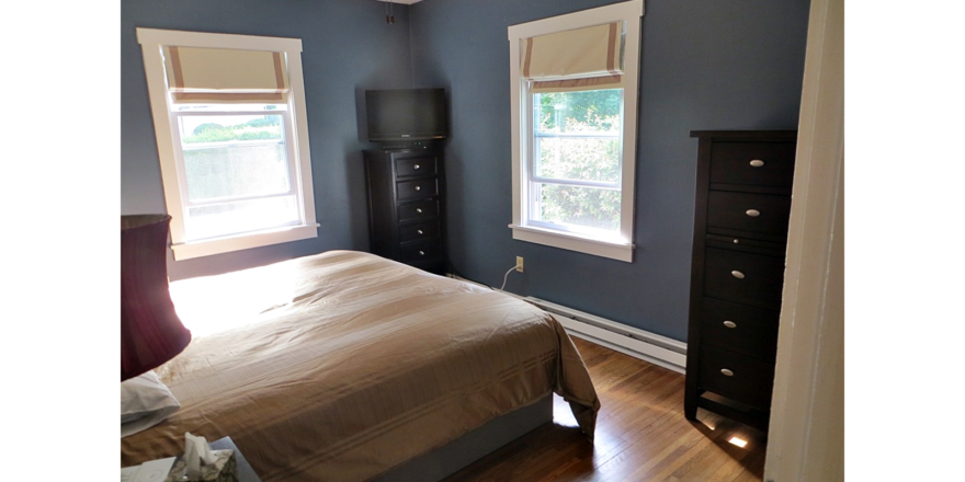 Bedroom with queen bed and two black dressers with 5 drawers. A TV is on top of one of the dressers.