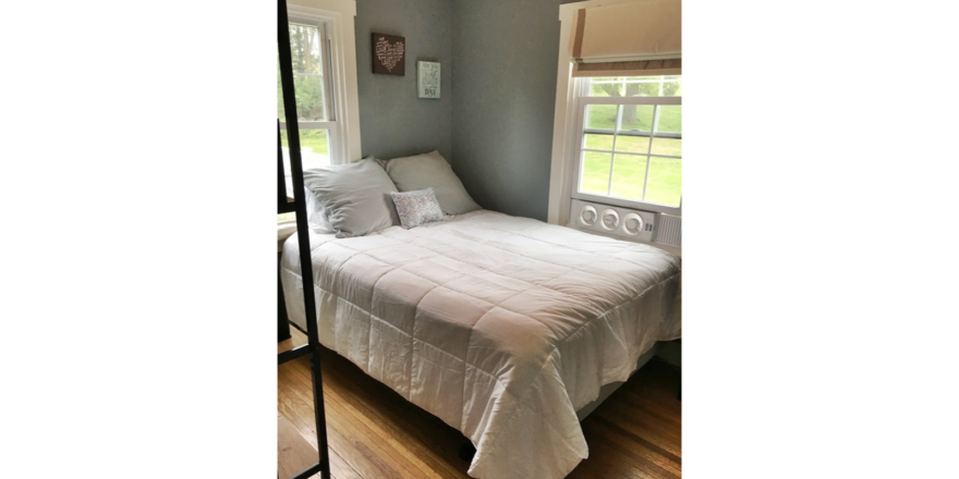 Bedroom with queen bed and window unit fan.