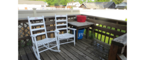 Wood deck with two white rocking chairs and wooden table.