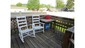 Wood deck with two white rocking chairs and wooden table.