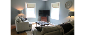 Living room with gray couch and love seat, industrial-style coffee table, two floor lamps and a TV