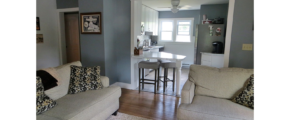 Kitchen with white cabinets and counter top, stainless steel appliances and living room with couch and loveseat