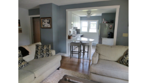 Kitchen with white cabinets and counter top, stainless steel appliances and living room with couch and loveseat