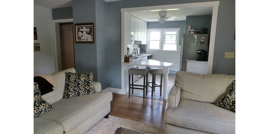 Kitchen with white cabinets and counter top, stainless steel appliances and living room with couch and loveseat