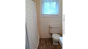 Bathroom with wood-style floor, toilet, shower with curtain, and window
