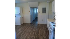 Kitchen with wood-style floor, stackable washer/dryer, white appliances, white cabinets, and light-colored countertops