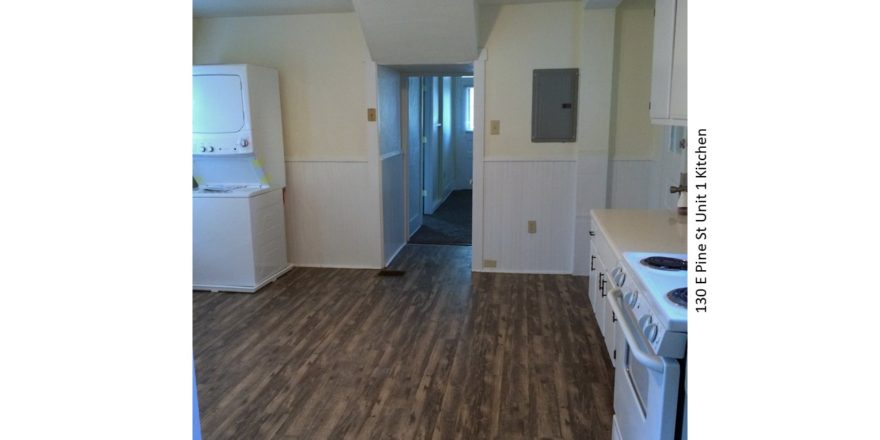 Kitchen with wood-style floor, stackable washer/dryer, white appliances, white cabinets, and light-colored countertops