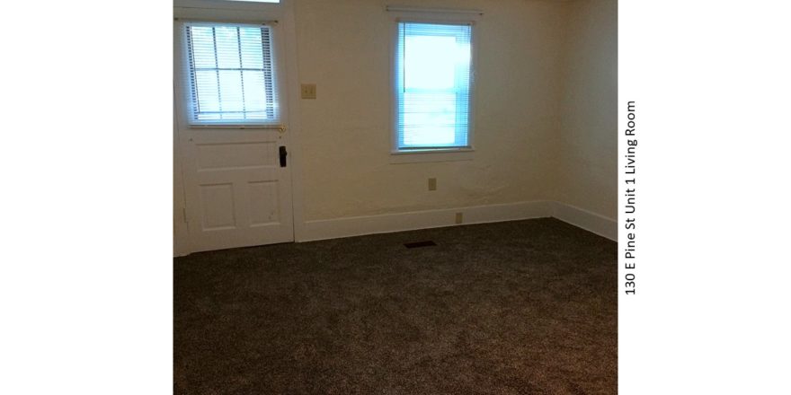 Unfurnished, carpeted living room with window and front door