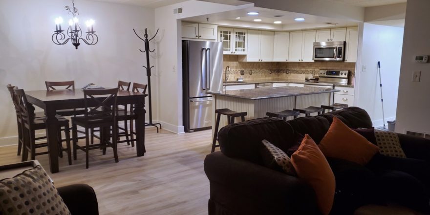 Kitchen with stainless steel appliances and white cabinets, and furnished dining area and living room