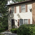 Exterior of a townhome with off-white siding and brown shutters.