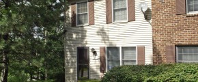 Exterior of a townhome with off-white siding and brown shutters.