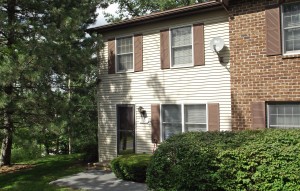 Exterior of a townhome with off-white siding and brown shutters.