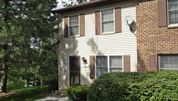 Exterior of a townhome with off-white siding and brown shutters.