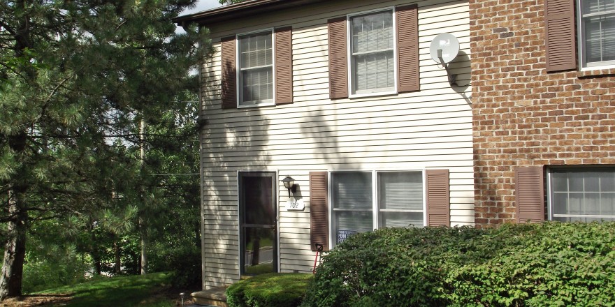 Exterior of a townhome with off-white siding and brown shutters.