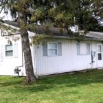 Exterior of ranch house with small lawn, light vertical siding, and pale blue shutters.