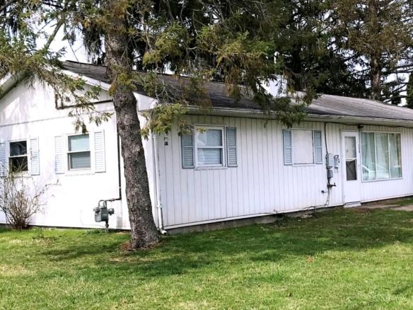 Exterior of ranch house with small lawn, light vertical siding, and pale blue shutters.