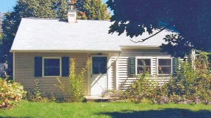 Exterior of small, one-story home with light siding and green shutters