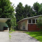 Carport with white and blue siding and ranch house with tan siding and brick walls