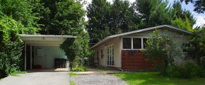 Carport with white and blue siding and ranch house with tan siding and brick walls