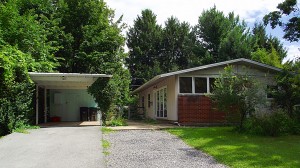 Carport with white and blue siding and ranch house with tan siding and brick walls