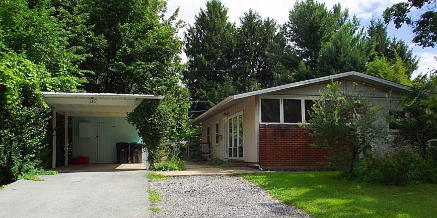 Carport with white and blue siding and ranch house with tan siding and brick walls