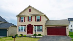 Exterior of two story house with large garage, tan siding and maroon front door, shutters, and garage door