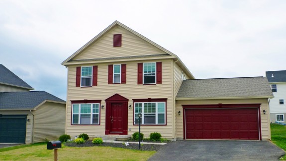 Exterior of two story house with large garage, tan siding and maroon front door, shutters, and garage door