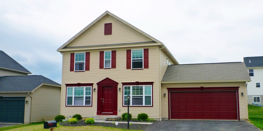 Exterior of two story house with large garage, tan siding and maroon front door, shutters, and garage door