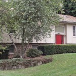 Exterior of house with tan siding, red front door, lawn, and landscaping