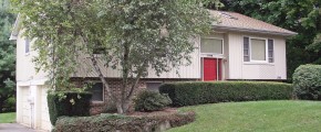 Exterior of house with tan siding, red front door, lawn, and landscaping