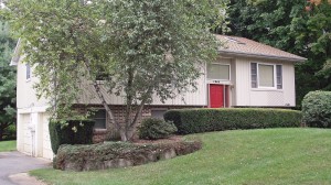 Exterior of house with tan siding, red front door, lawn, and landscaping