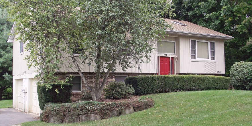 Exterior of house with tan siding, red front door, lawn, and landscaping