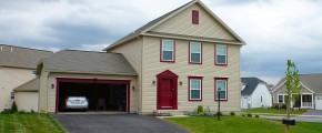 Exterior of house with tan siding, red front door, garage door, and trim, driveway, and lawn