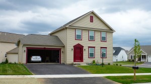 Exterior of house with tan siding, red front door, garage door, and trim, driveway, and lawn
