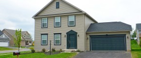 Exterior of house with tan siding, green front door, garage door, and trim, driveway, and lawn