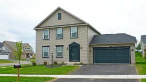 Exterior of house with tan siding, green front door, garage door, and trim, driveway, and lawn