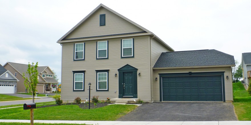 Exterior of house with tan siding, green front door, garage door, and trim, driveway, and lawn