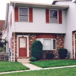 Exterior of townhouse with brick first floor and light gray siding with red shutters on the second floor