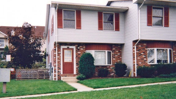 Exterior of townhouse with brick first floor and light gray siding with red shutters on the second floor