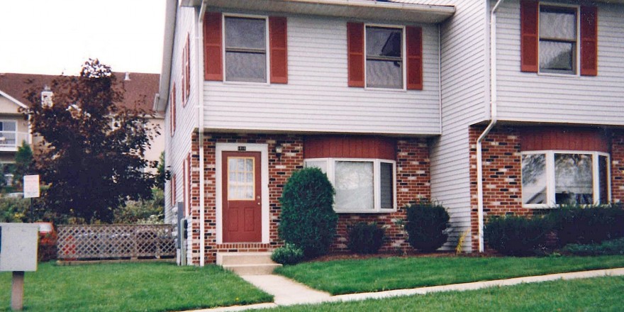 Exterior of townhouse with brick first floor and light gray siding with red shutters on the second floor