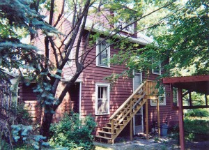 Exterior of house with red siding and light wood stairs up to one entrance