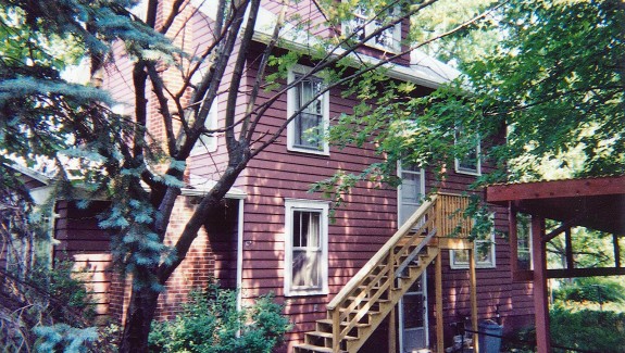 Exterior of house with red siding and light wood stairs up to one entrance