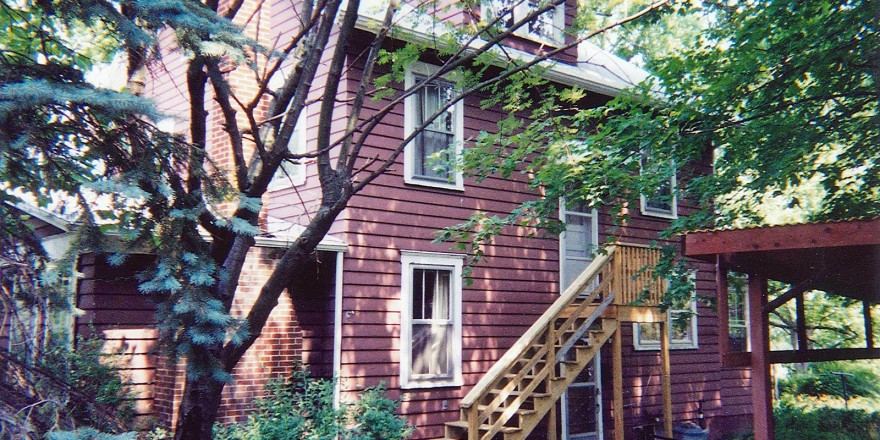 Exterior of house with red siding and light wood stairs up to one entrance